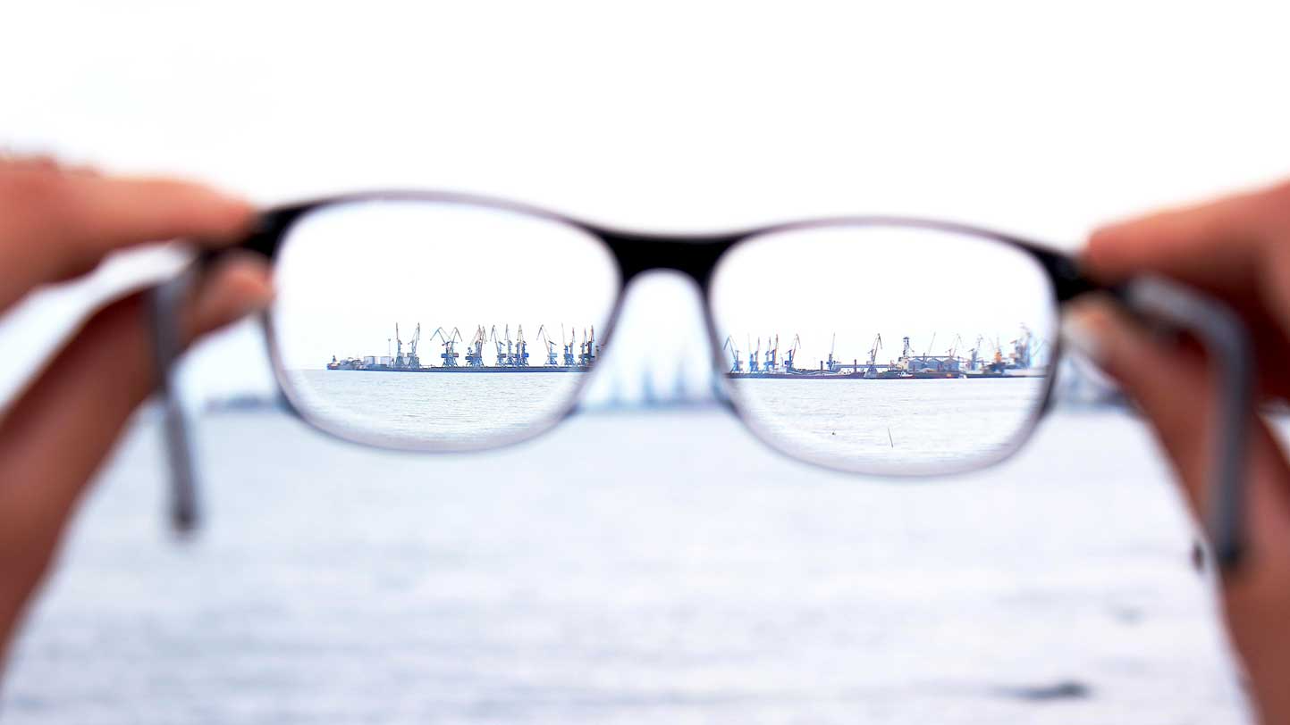 Primer plano de unas gafas enfocando un puerto, simbolizando la visión clara y la protección del patrimonio, con un mensaje que destaca el papel de los guías y guardianes en la seguridad patrimonial y el futuro.