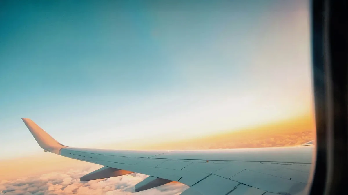 Vista del ala de un avión sobre las nubes durante un atardecer, con un cielo claro y tonos anaranjados y azules, simbolizando el viaje hacia Uruguay, un destino para nómadas digitales.