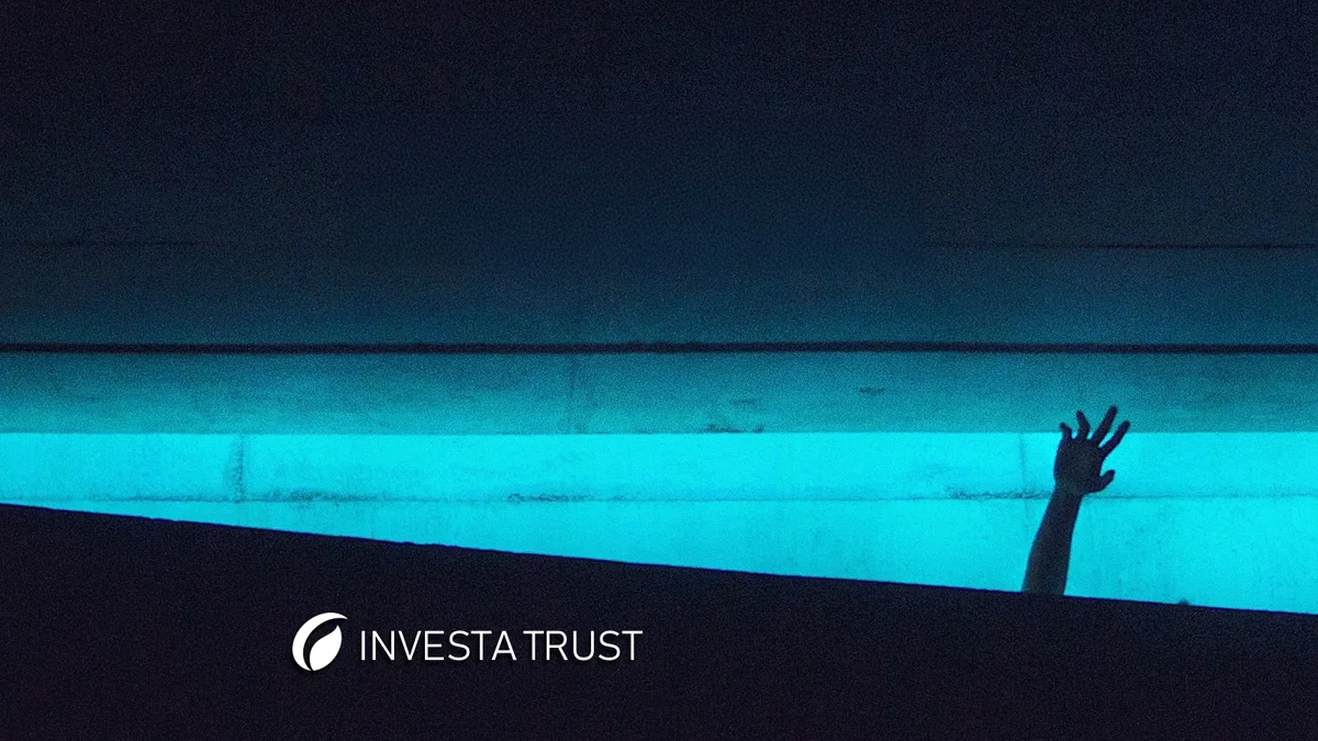 Mano levantada en un ambiente oscuro con iluminación azul, con el logo de Investa Trust.