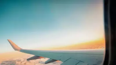 Vista del ala de un avión sobre las nubes durante un atardecer, con un cielo claro y tonos anaranjados y azules, simbolizando el viaje hacia Uruguay, un destino para nómadas digitales.