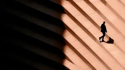 Persona caminando entre luces y sombras de un edificio, símbolo de movilidad y planificación patrimonial internacional.