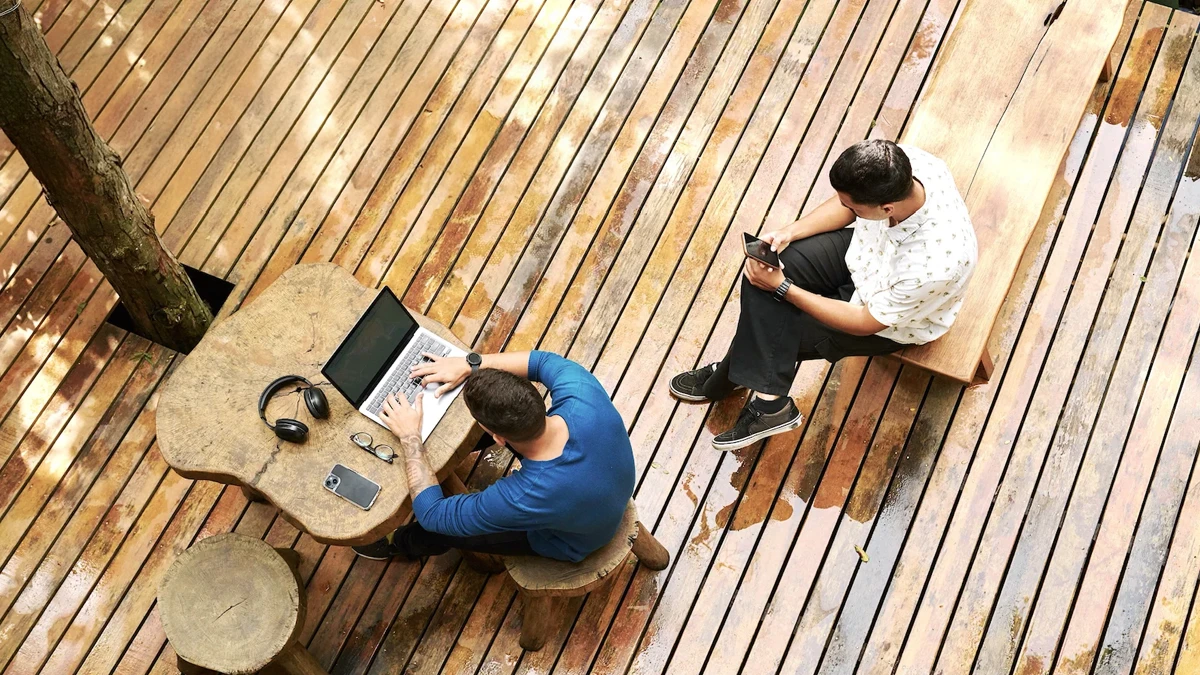 Vista aérea de dos personas trabajando al aire libre, una en una laptop y la otra en un dispositivo móvil, simbolizando la planificación y gestión de riesgos en empresas familiares en un entorno colaborativo.